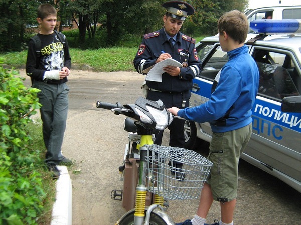 Сотрудник ДПС выписывает штраф ребятам на электромотоцикле