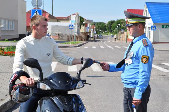 Молодой человек на скутере передает водительское удостоверение сотруднику государственной автоинспекции