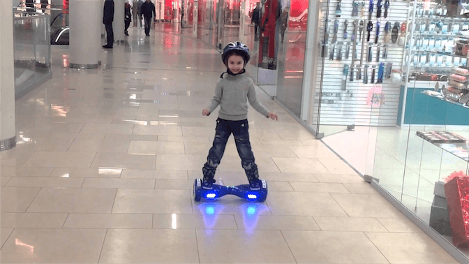 ребенок в шлеме катается на гироскутере в торговом центре
