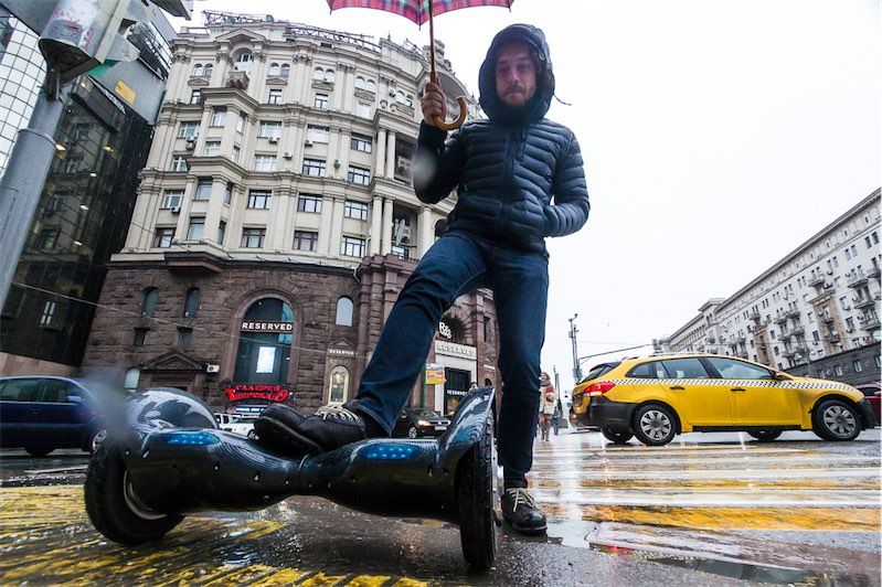 человек с зонтом едет по дождливому городу на гироскутере